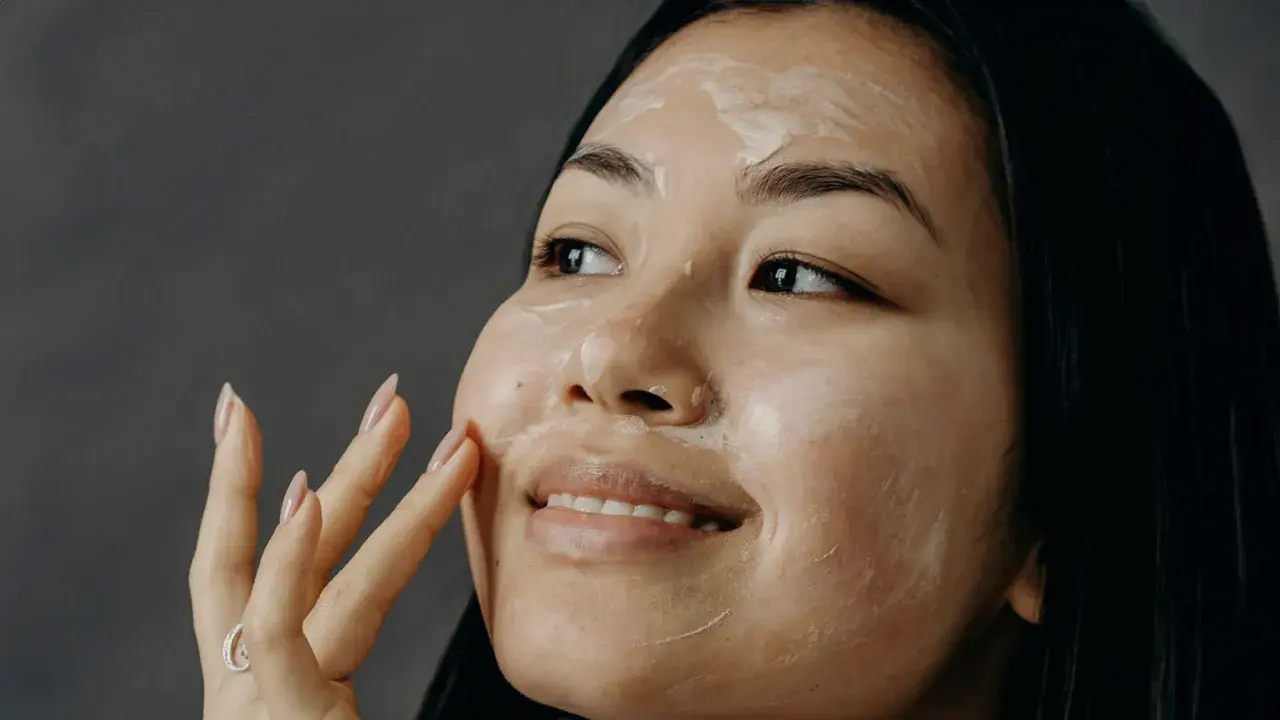 Una donna applica una crema sul viso, un gesto che racchiude l'essenza di che cos'è la skincare: cura e benessere per la pelle.