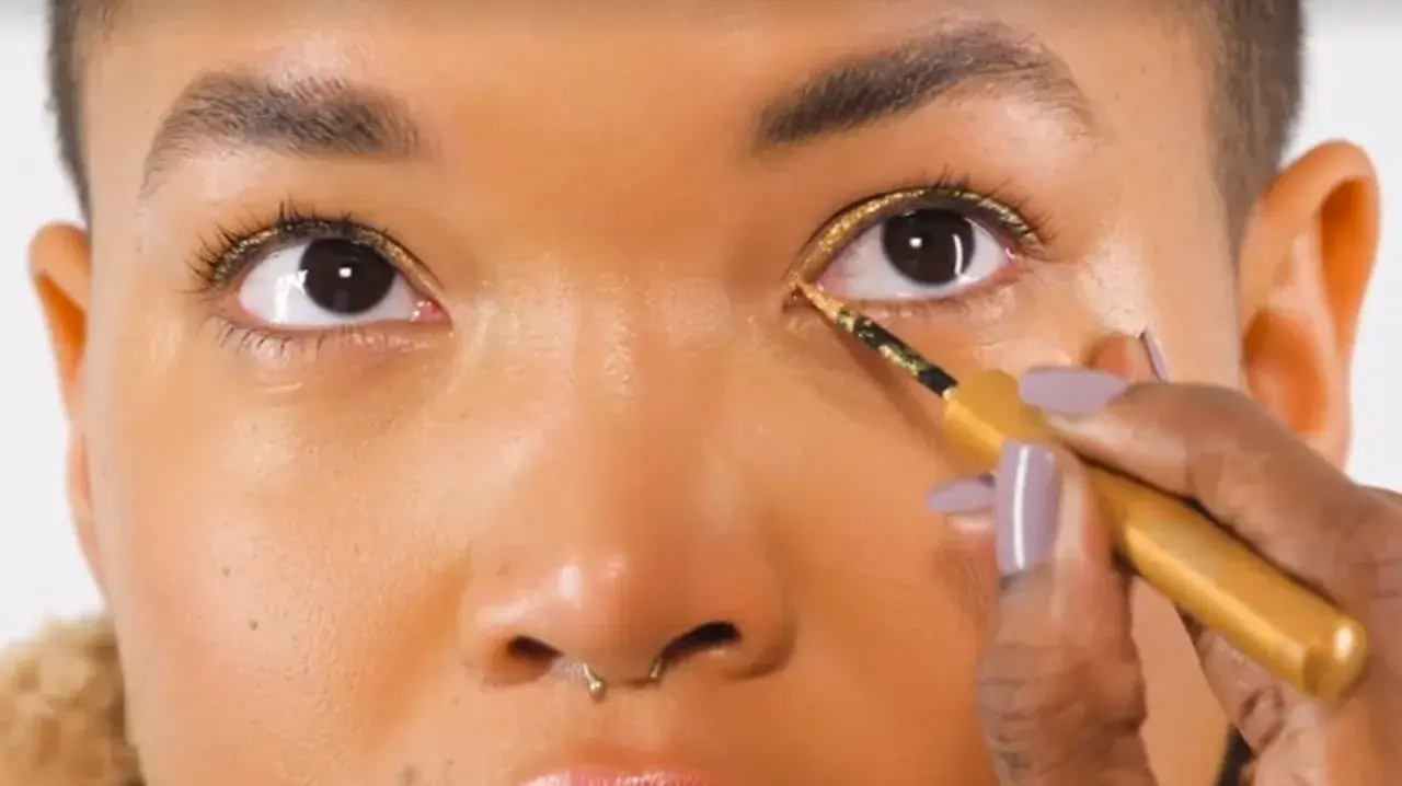 Occhi illuminati da un trucco oro e marrone scintillante, con eyeliner dorato applicato con precisione.