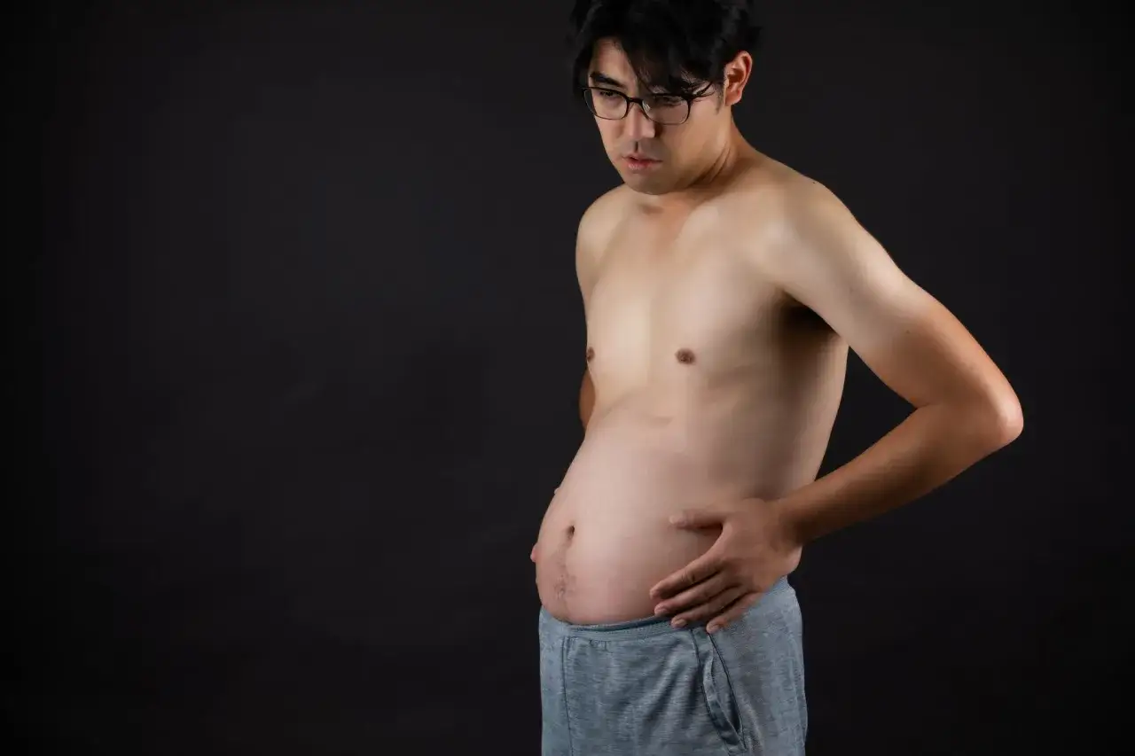 Uomo magro con pancia gonfia, che si tocca l'addome con preoccupazione.