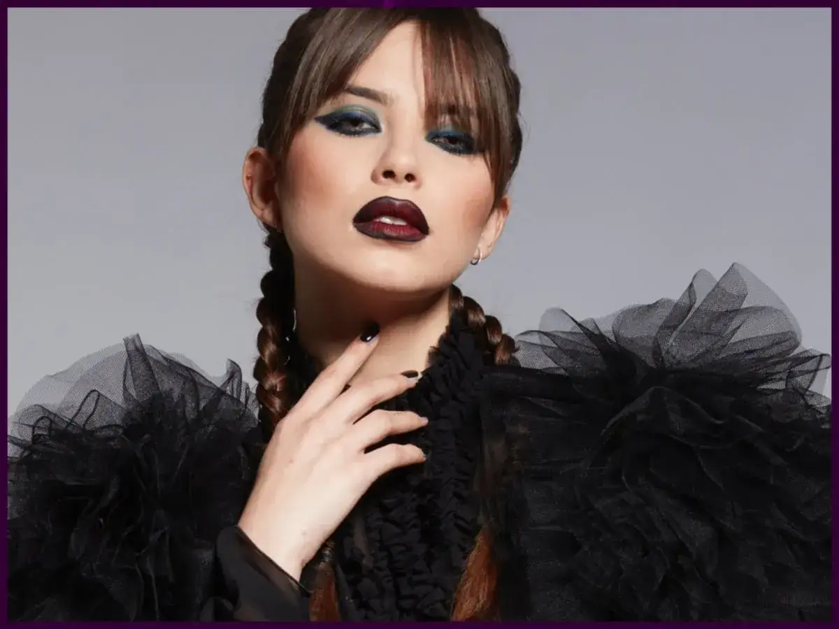 Donna con trucco halloween: occhi scuri, labbra bordeaux, trecce e abito nero voluminoso.