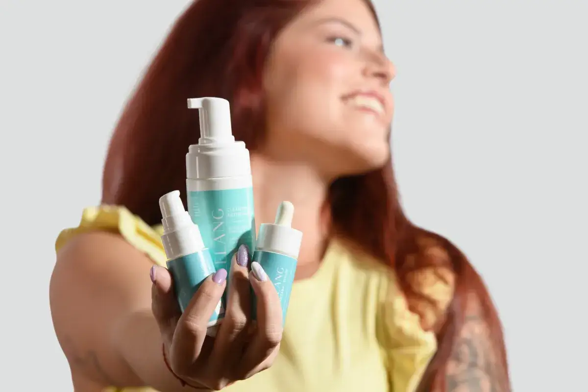 Donna sorridente mostra tre prodotti per il trattamento pelle grassa: una mousse detergente e due sieri.