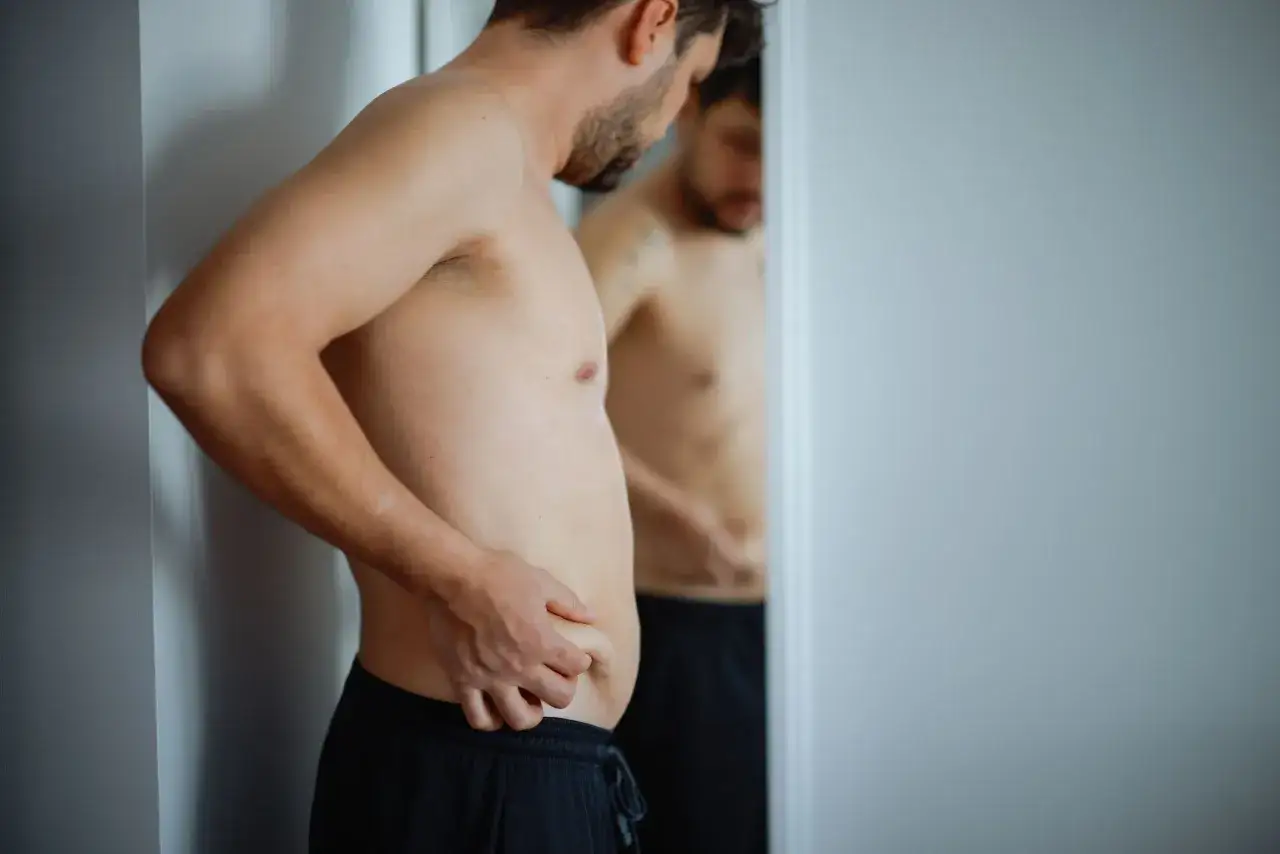 Uomo si guarda allo specchio, preoccupato per il gonfiore addominale. Il cortisolo gonfia, e lui lo sente.