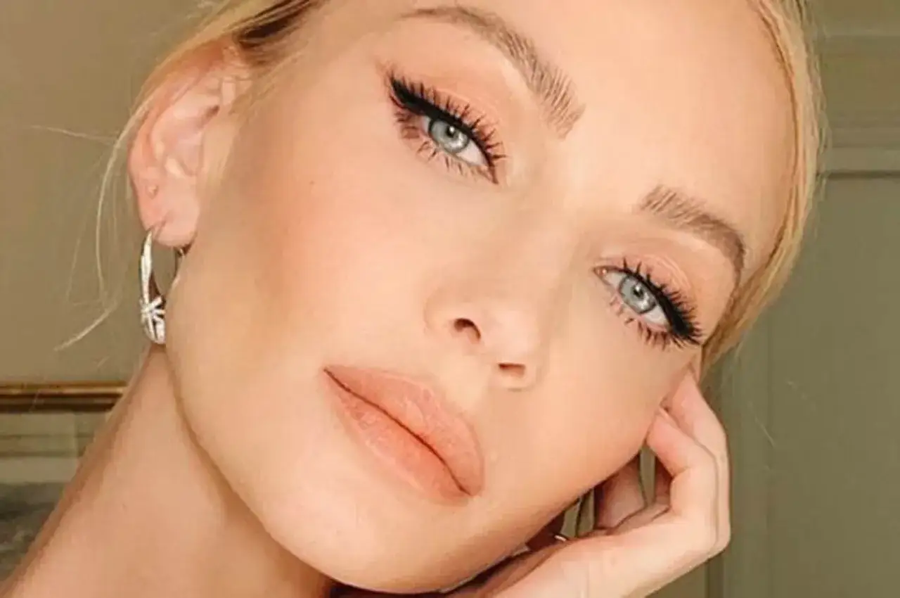 Un elegante trucco occhi azzurri con eyeliner e ciglia lunghe, labbra nude e orecchini a cerchio.
