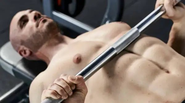 Uomo a petto nudo si allena con bilanciere, un passo fondamentale per chi vuole imparare come aumentare la massa muscolare.