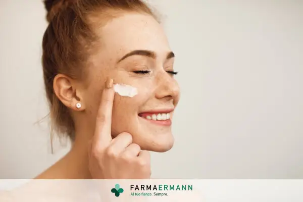 Donna sorridente applica latte detergente viso con la mano.