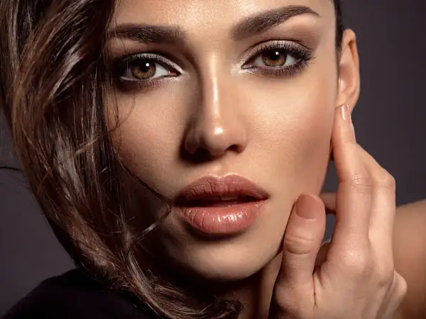Close-up of a woman's face with dark eye makeup, glossy lips, and brown hair.