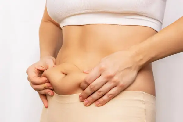 Mani che stringono il fianco, mostrando accumuli di grasso. Il cortisolo gonfia, evidenziando la necessità di uno stile di vita sano.
