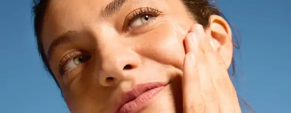 Dita accarezzano il viso per una pelle perfetta, illuminata dal sole.