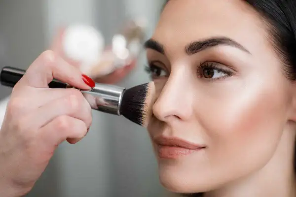 Mano con pennello applica terra sul viso per un look impeccabile.