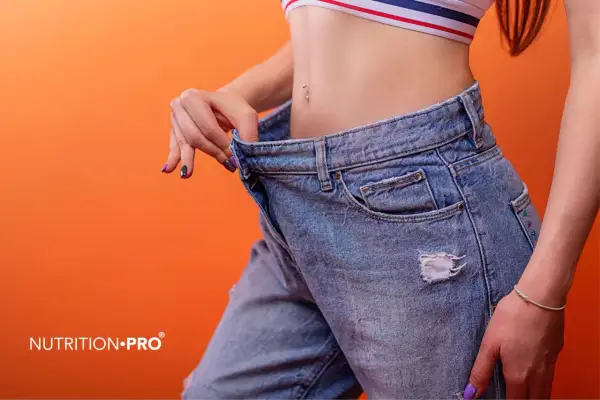 Donna mostra jeans larghi, segno di successo nel come appiattire la pancia. Un risultato visibile di un percorso di benessere.