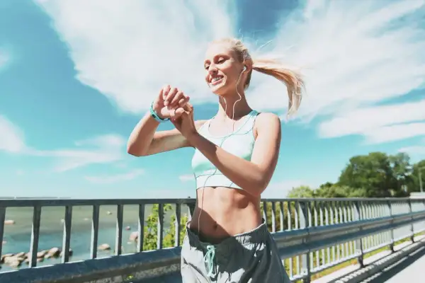 Donna bionda con smartwatch e auricolari controlla i suoi progressi, ideale per dimagrire meglio correre o camminare.
