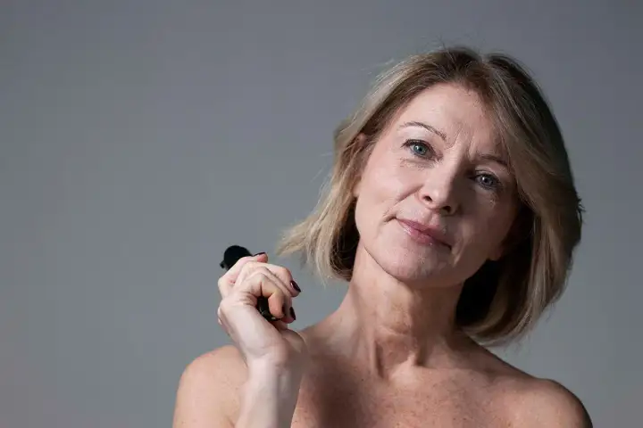Donna con pelle cadente sotto il mento, che tiene un piccolo oggetto nero. Scopri i rimedi per la pelle cadente sotto il mento.